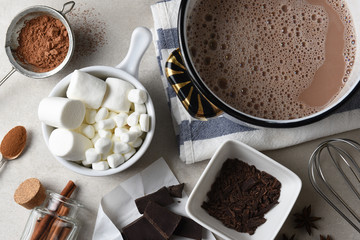 Overhead shot of the ingredients and tools, for making hot cocoa. A pot of cocoa with marshmalllows, cunnamon, star anise, shaved chocolate