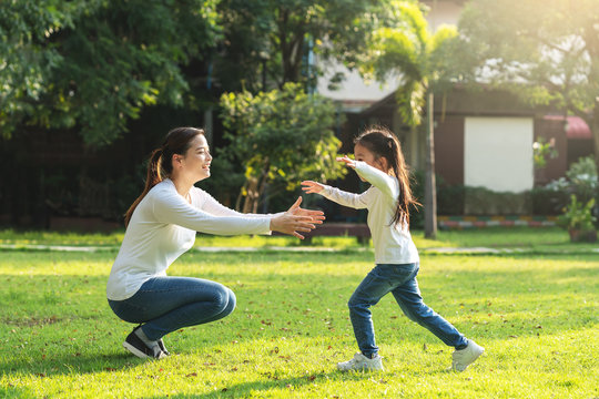 Attractive Young Asian Mother And Little Cute Girl Daughter Run To Hug Her Mom In Garden After Back School In Evening. Mom And Kids Feeling Relax Enjoy Playing Outside Concept. Bonding In Asia Family.