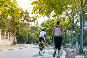 Fototapeta premium Sporty Caucasian woman running on the road in the Asian city park with green tree row in early morning