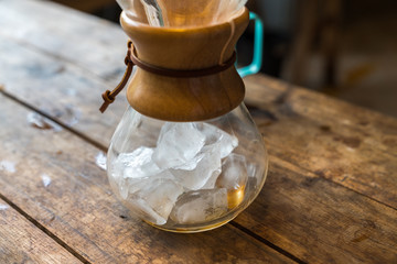 Glass bottle with ice to make ice drip coffee, on wooden table, vintage style