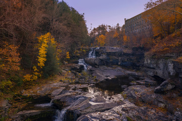 autumn waterfall scene with trees and old building in background