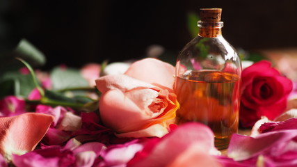 Aroma oil glass bottle among roses and petals on the table, natural raw material, selected focus