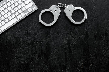 Cyberfraud concept. Handcuff near keyboard on black background top view copy space