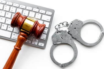 Arrest of a hacker for cyber fraud concept. Handcuff near keyboard and judge gavel on white...