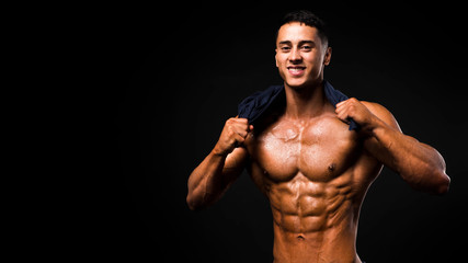 Portrait of handsome muscular guy with towel in the neck posing over a dark background.