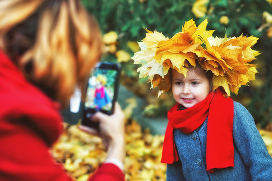 mom takes pictures of her daughter with a mobile phone in the autumn Park