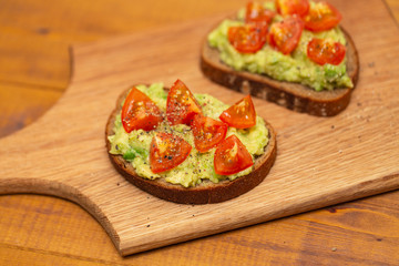 Avocado toast with cherry tomatoes on wooden background. Breakfast with avocado toast, vegetarian food.