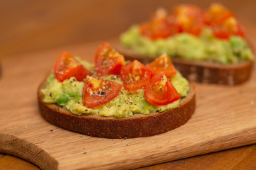 Avocado toast with cherry tomatoes on wooden background. Breakfast with avocado toast, vegetarian food.