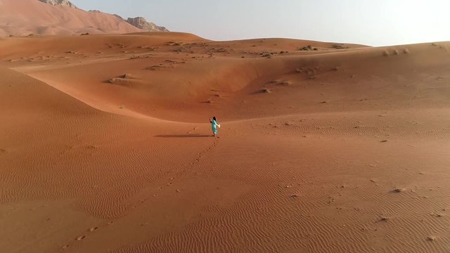 Aerial view of woman walking and making photo in desert, Dubai, UAE.