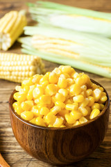 Canned corn in a wooden plate and cob of fresh corn on a rustic wooden background