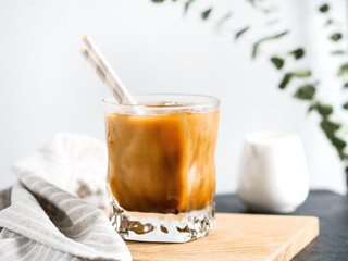 Refreshing iced latte coffee in a glass with straws in a modern kitchen.
