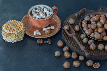 on the table on a wooden stand hazelnuts, waffles and a cup of hot chocolate with marshmallows close-up