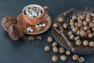 Hazelnuts, muffins and a cup of hot chocolate with marshmallow , on a table on a wooden stand