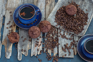on the wooden table, coffee beans, two cups of coffee and muffins - background about dessert and rest