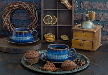 on the table are coffee in blue ceramic cups, muffins and an old coffee grinder