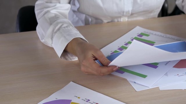 Above view dolly shot of graphic data templates on long table with unrecognizable business woman analyzing them