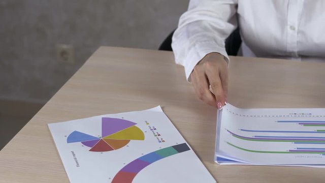 Above view dolly shot of graphic data templates on long table with unrecognizable business woman analyzing them