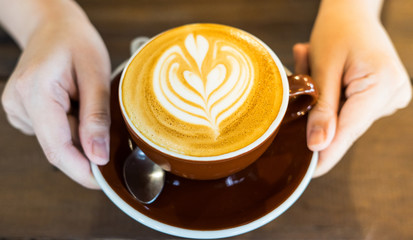 Close up of female hand serving coffee with latte art in the morning. Focus on female hands placing a cup of coffee.
