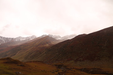 Mountains in autumn with brown and reddish grass under cloudy sky