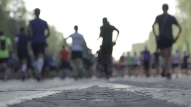 Low angle slow motion shot of marathon runners viewed from behind, right after the start
