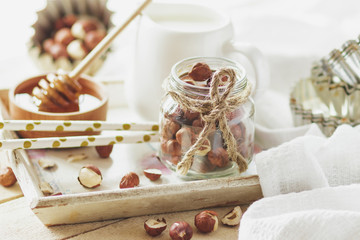 Honey in the wooden bowl, hazelnuts and jar with milk on the wooden tray