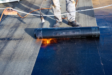 Worker preparing part of bitumen roofing felt roll for melting by gas heater torch flame