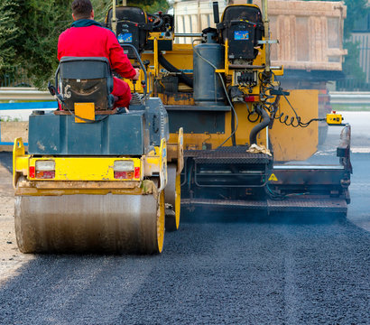 Worker leads the vibrating road roller to compact the asphalt laid out for the construction of a road