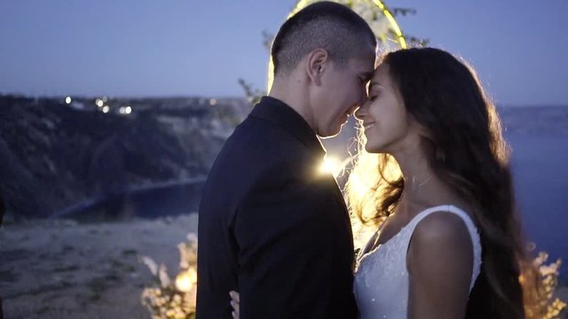 Side view of young married couple standing and kissing on background of chancel in the evening in Crimea
