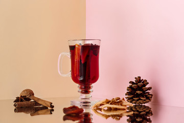 Mulled wine in glass with cinnamon stick, christmas sweets on on the glass table and fruits and...