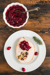 Stuffed  turkey breast roll with cranberry sauce on white plate on rustic wooden table, top view