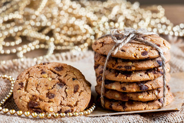 Chocolate chip cookies freshly baked are stacked on sackcloth with christmas lights in the background. Christmas cookies. Homemade pastry.