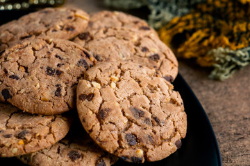 Chocolate chip cookies freshly baked are pile on black plate with scarf on wooden table background. Christmas cookies. Homemade pastry.