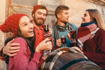Smiling european men and women during party photoshoot. The guys posing as friends at studio fest with wineglasses with hot mulled wine on foreground.