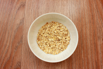 Oat flakes in a white bowl on wood  brown
