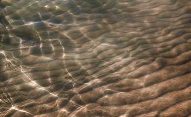 Fototapeta na wymiar Top view of texturized river bottom shining through glittering shallow water.
