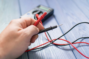 Electronic multimeter to measure the current in a male hand on a wooden background.