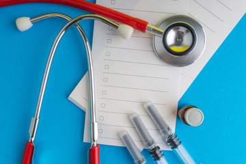 Medical syringe, stethoscope, vials, ampule and notebook on blue background with selective focus and crop fragment