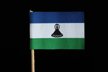 A official and original flag of Lesotho on toothpick on black background. A horizontal triband of blue, white and green with black mokorotlo centred on the white band