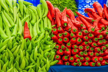 Red and green peppers on sale in a market, with one misplaced pepper..