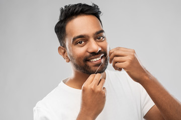 oral care, hygiene and people concept - smiling young indian man with dental floss cleaning teeth...