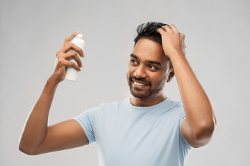 grooming, hairstyling and people concept - happy smiling indian man applying hair spray over gray...