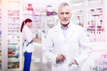 Confident grey-haired pharmacist holding his hand in the pocket