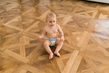 Beautiful cute naked baby sitting on the wooden floor wearing only cloth diaper.