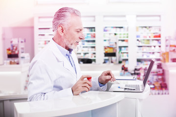 Naklejka na ściany i meble Elder grey-haired pharmacist working with a laptop