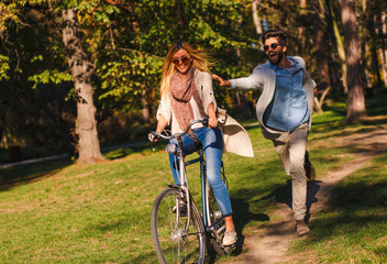 Happy young couple having fun riding a bicycle on sunny day in the park.