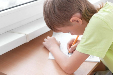 School child boy learns to write letters sitting by the table. Doing homework.