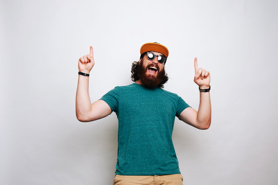 Cheerful amazed bearded man pointing up over white background