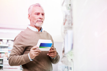 Pondering elder client carrying a package of prescribed pills