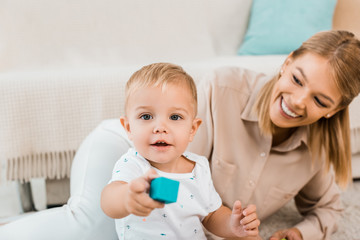 adorable toddler looking at camera and playing with colorful cube and mother