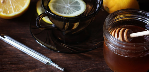 Drugs and pills on a wooden table. Various means to prevent colds. Tea with lemon and honey. Glass cup with tea slice of lemon and jar of honey.